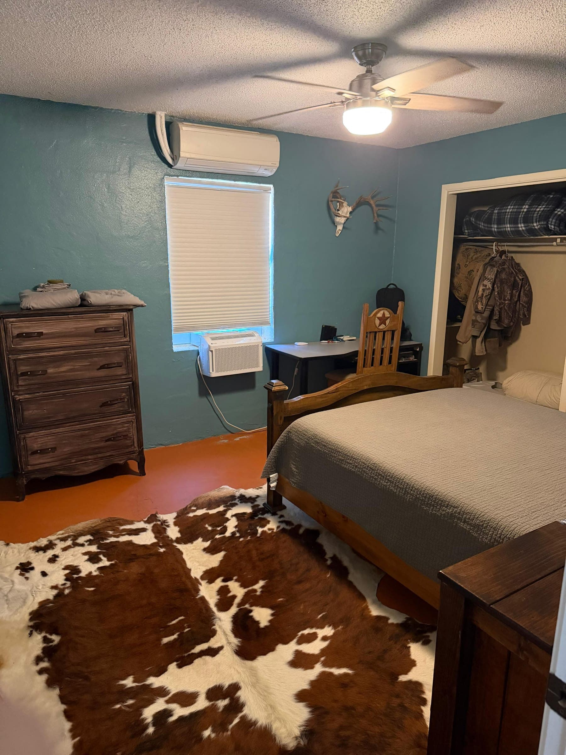 A lodge bedroom with a cowhide rug, a made bed and a wooden dresser