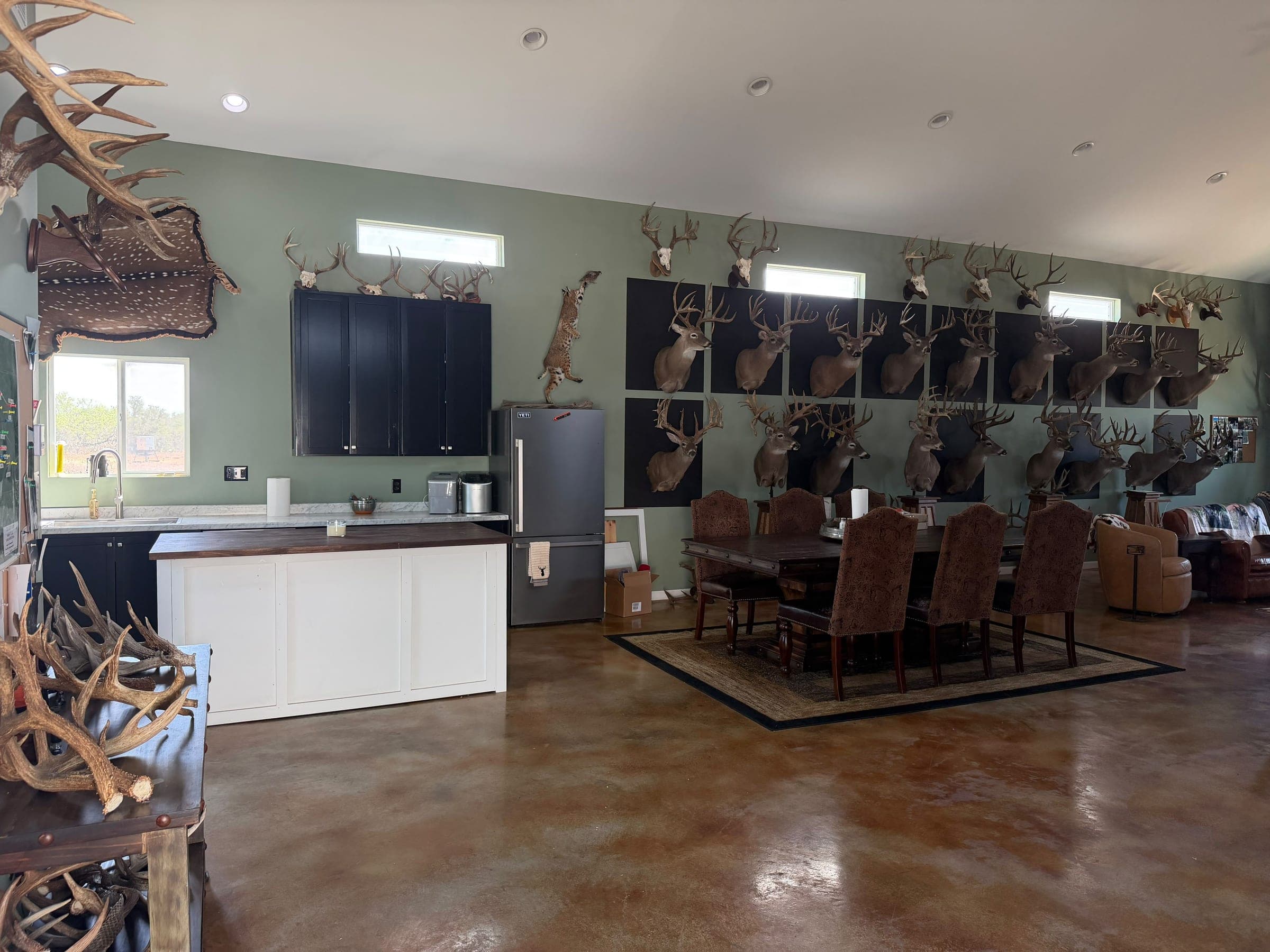 The lodge great room: an open kitchen and a long dining table under walls hung with mounted trophies