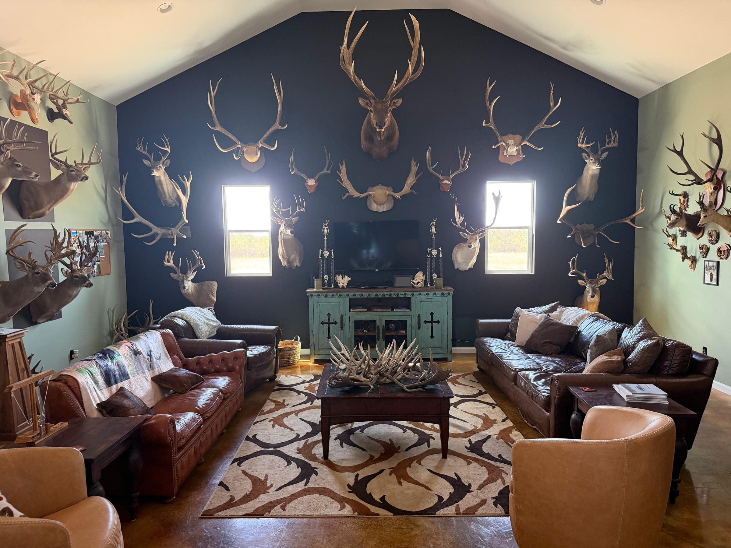 The lodge living room: leather sofas facing a dark wall hung with mounted trophies