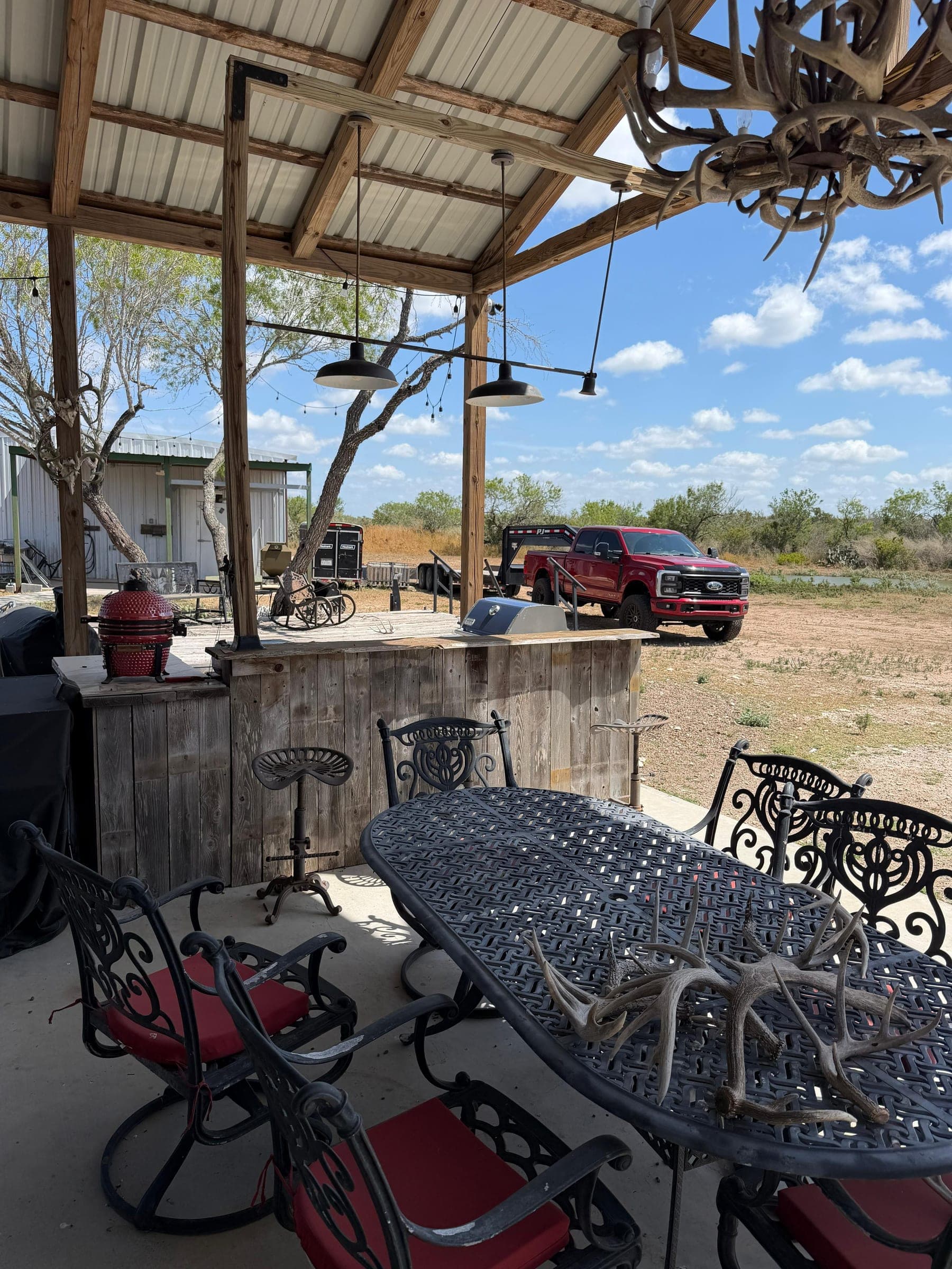 The covered patio at the lodge: an outdoor dining table under an antler chandelier, brush country beyond