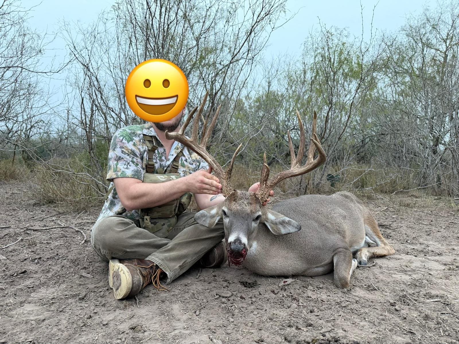Hunter seated beside a harvested whitetail buck in the brush