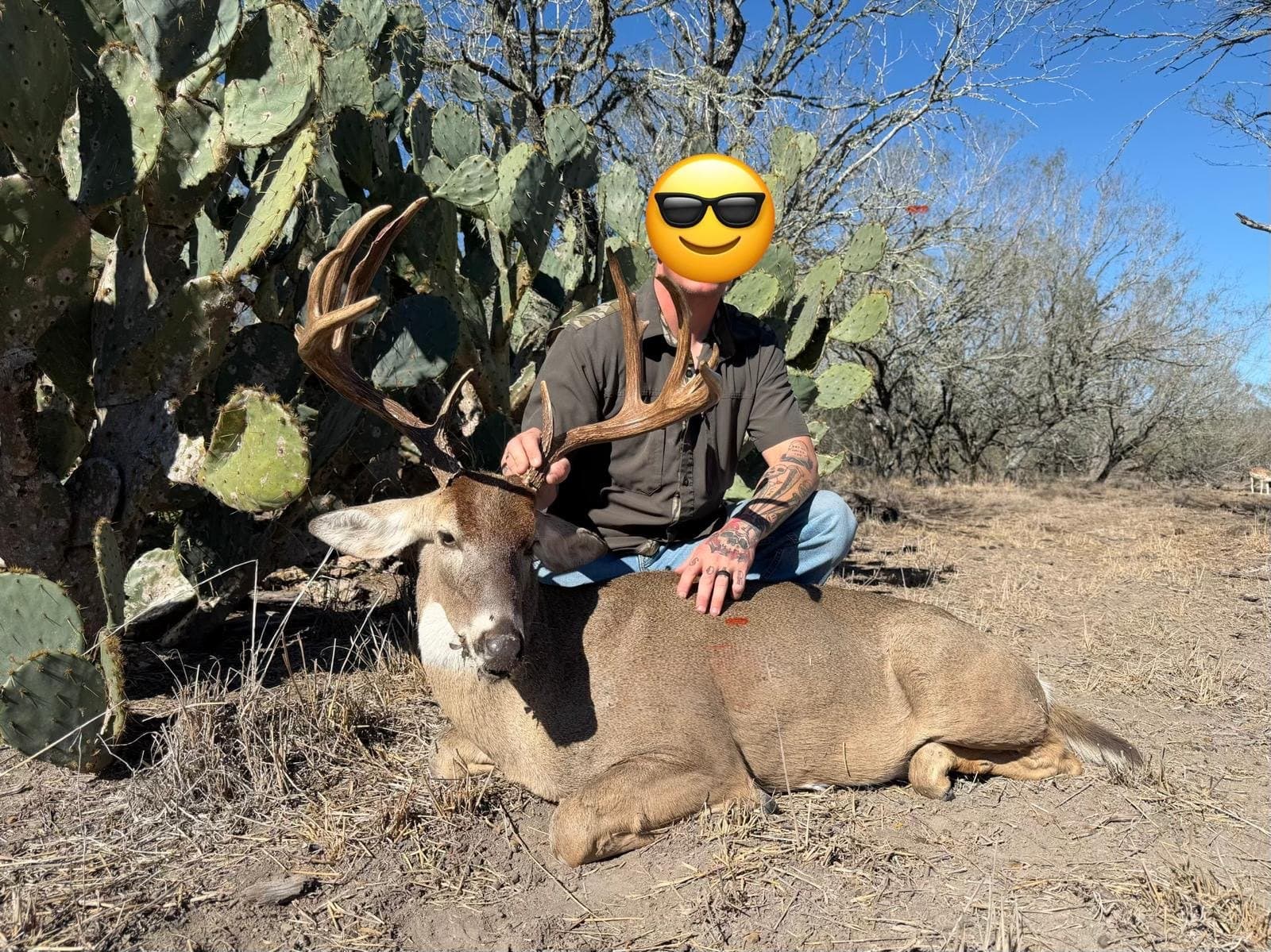 Hunter beside a harvested whitetail buck in front of prickly pear cactus