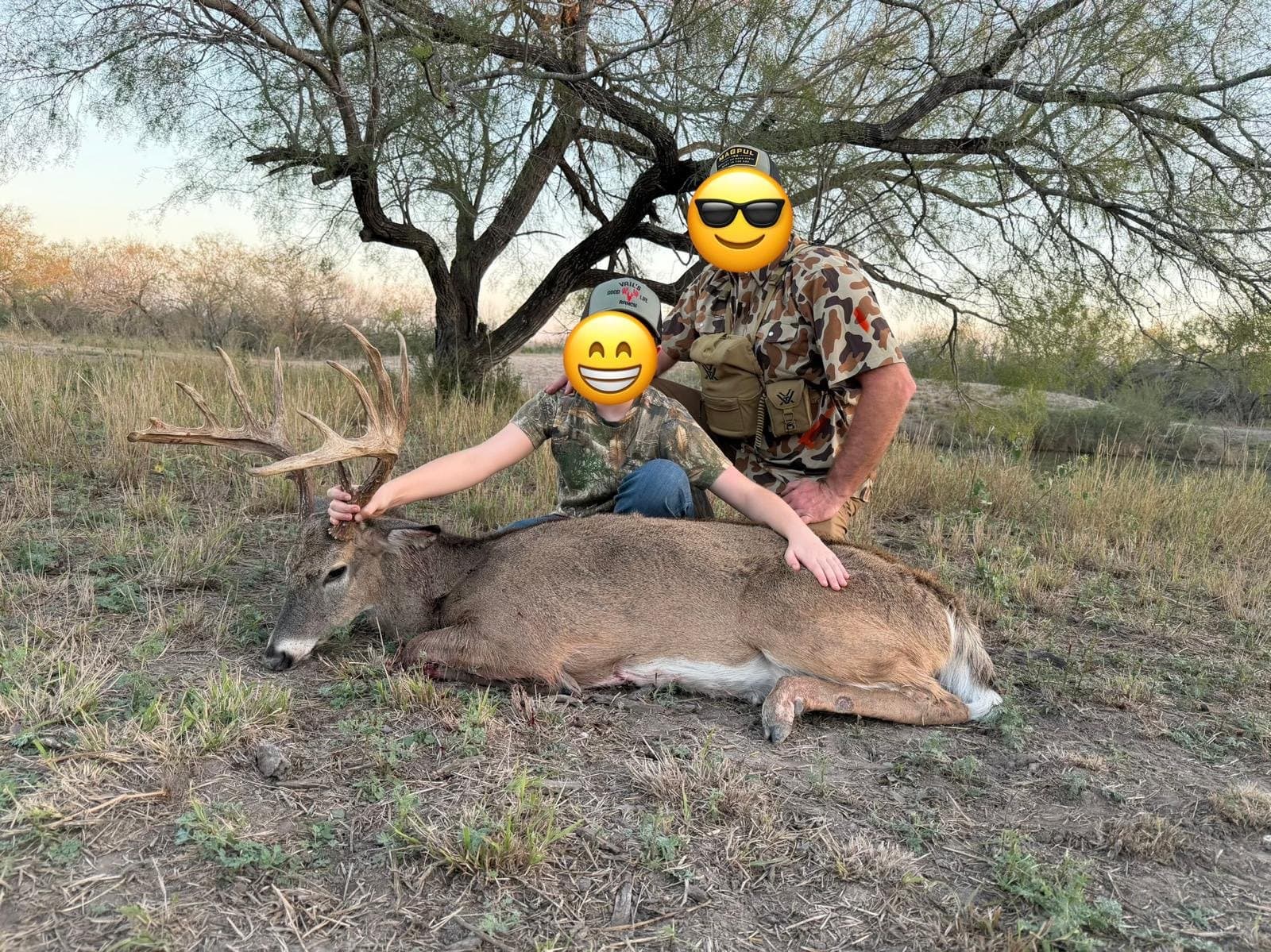 Adult and young hunter seated behind a harvested whitetail buck at sunset