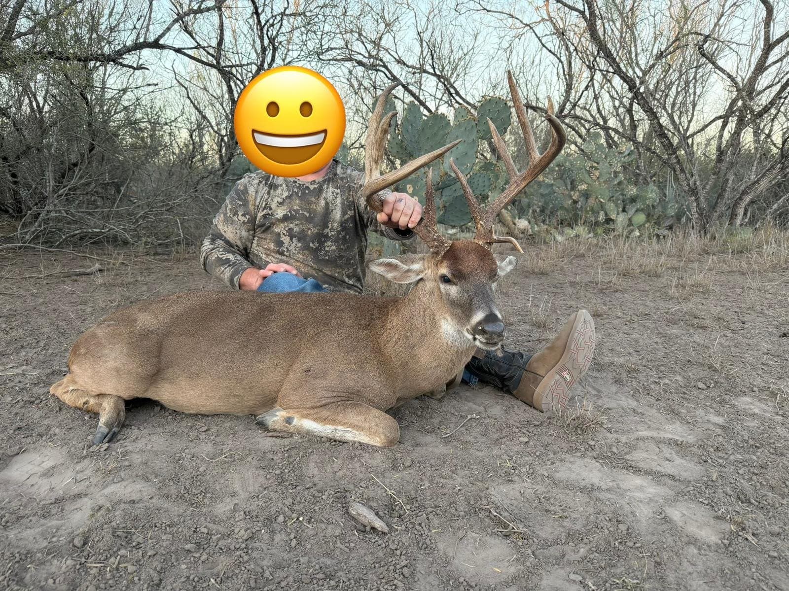 Hunter seated behind a harvested whitetail buck on a sandy sendero