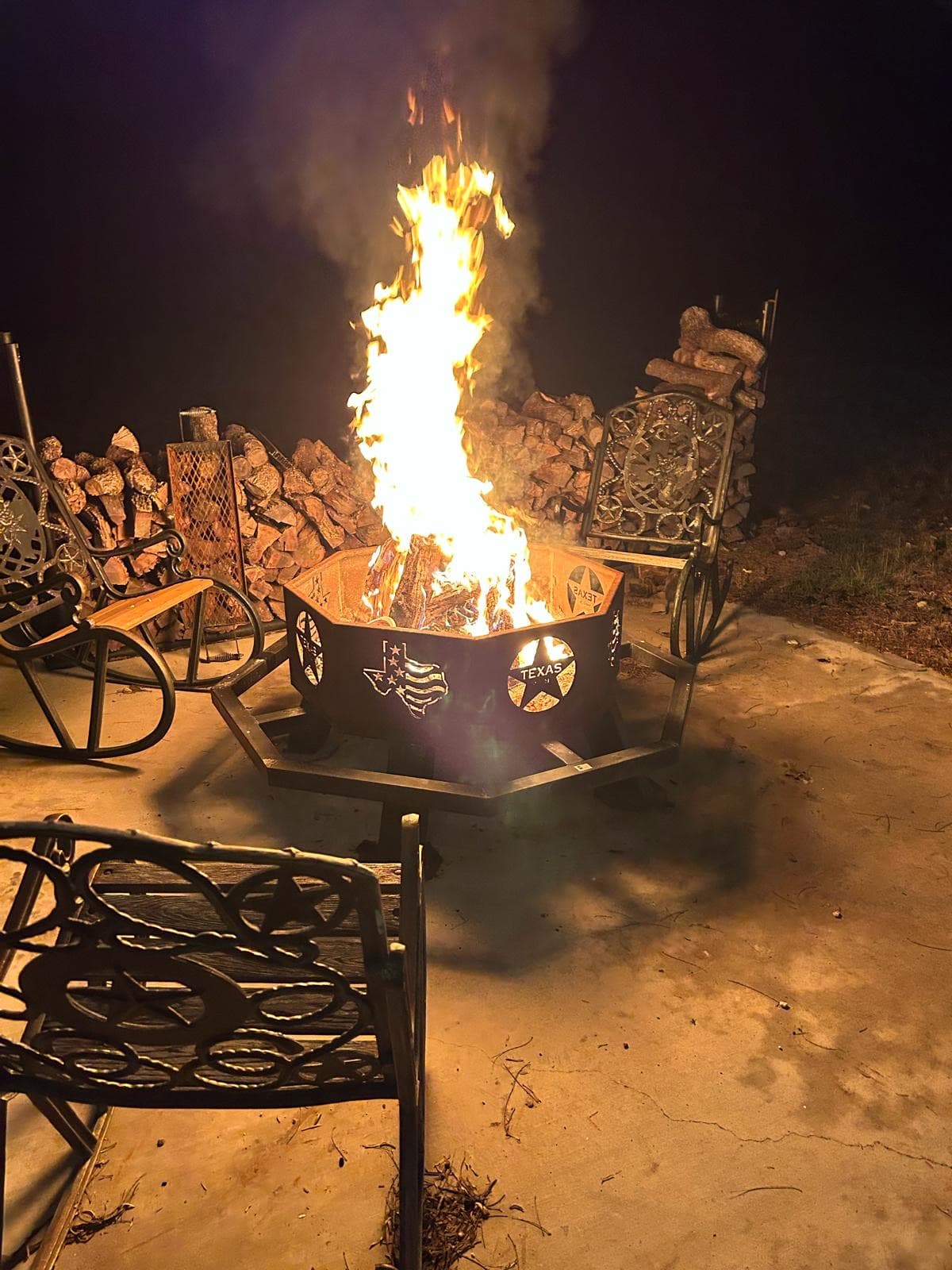 A fire burning in a Texas star fire ring on the lodge patio after dark, chairs pulled up around it